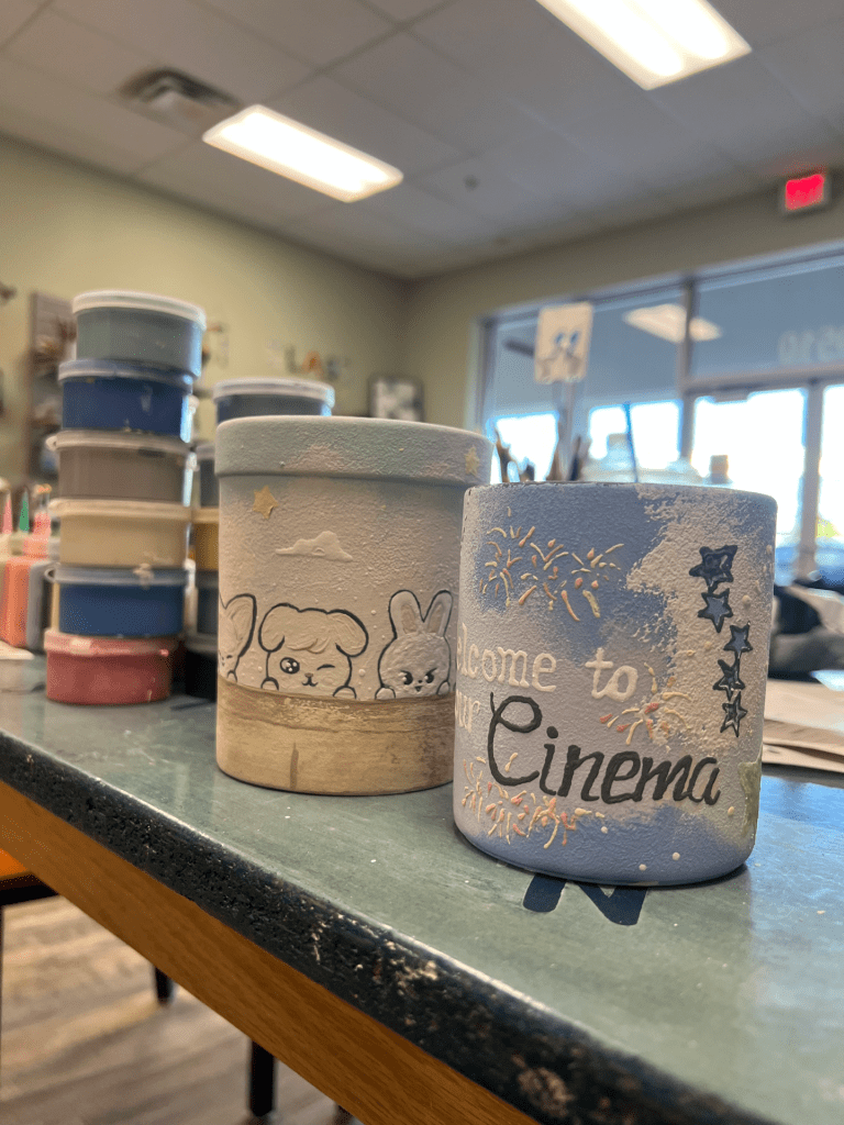 Image of fully painted ceramics on a table with stack of paint/glaze beside.
